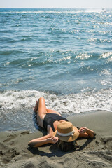 Woman sunbathing on sandy beach in swimsuit and straw hat, Ulcinj, Montenegro