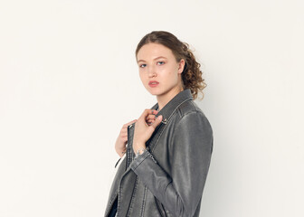 a woman dressed in accordance with fashion trends, in a leather jacket and a white top poses...