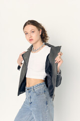 A stylish woman in a leather jacket with a white eco-leather bag and curly hair poses against a...