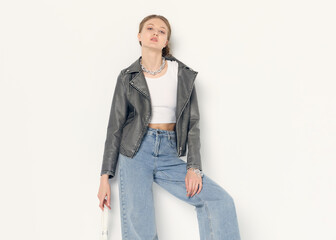 a woman dressed in accordance with fashion trends, in a leather jacket and a white top poses...