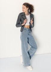 a woman dressed in accordance with fashion trends, in a leather jacket and a white top poses...