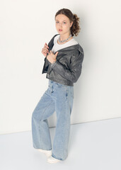 a woman dressed in accordance with fashion trends, in a leather jacket and a white top poses...