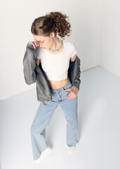 a woman dressed in accordance with fashion trends, in a leather jacket and a white top poses...