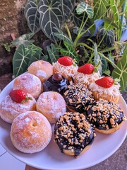 Assorted donuts on a white plate, topped with powdered sugar, chocolate glaze, shredded cheese,...