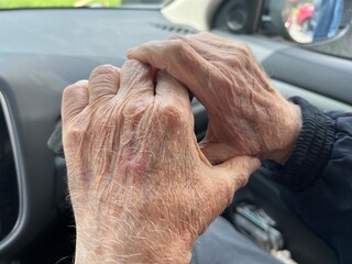 A close-up of an elderly man's wrinkled hands clasped together while holding a walking stick