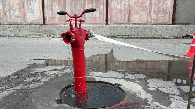 Close-up of a fire hydrant with a hose attached. Water flows from the opening of the fire hydrant. Fire department responds to a fire in the city