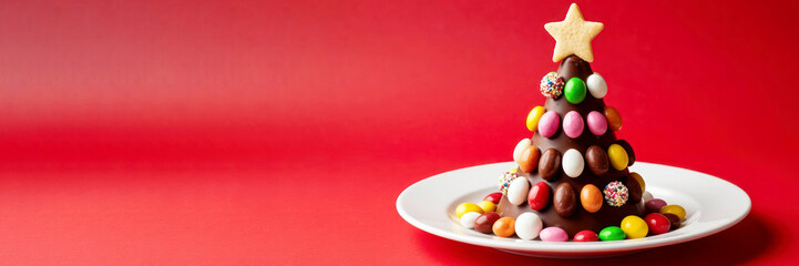 Obraz premium Chocolate Christmas tree made of candies and sugar decorations on a white plate with red background