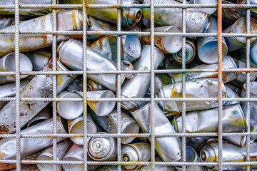 Variety of crushed cans collected in a mesh cage at a recycling facility on a sunny afternoon