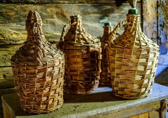 Handcrafted wicker bottles arranged on a rustic wooden table inside a traditional artisan workshop...