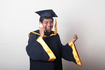 Young man dressed in cap and gown to celebrate his graduation uses his cell phone to take selfies, make calls and send messages at the prom