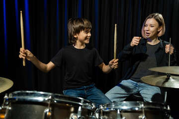 Young caucasian woman teaches a boy to play the drums in the studio on a black background. Music...