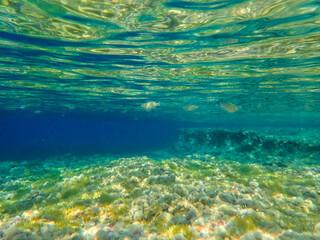 Dark blue ocean surface seen from underwater. Abstract waves underwater and rays of sunlight shining through, Sun light rays undersea deep, Underwater background with sea bottom, Mediterranean sea.