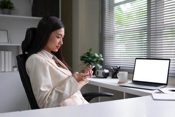 Young woman sitting on a chair with a smartphone, working from home, sending text messages,...