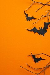 Halloween vertical composition with black paper bats and decorative branches on orange background, concepts of autumn, seasonal holidays and creative design. Top view, space for text