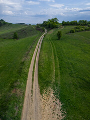 Aerial view of gravel road cutting through grass field near forest
