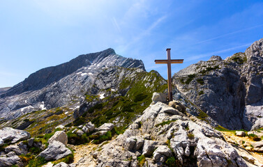A simple cross on the rocks with a mountain range on a beautiful summer sunny day in the Bavarian Alps