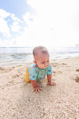 Jogja, indonesia-January 13, 2023. Asian toddler girl crawling happily on sandy beach with sea and hills behind. Fun childhood, tropical nature, family vacation, outdoor play, and carefree summer day.