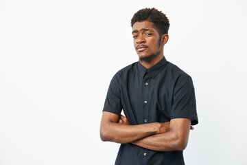 Confident black man with crossed arms, wearing a sleek black shirt against a plain background....