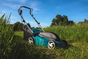 Fototapeta premium Electric lawn mower for cutting tall green grass in sunny field