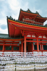Naklejka premium Countless white paper fortunes, or omikuji, are tied in rows before a vibrant red shrine building, a popular spiritual tradition representing the hopes and prayers of visitors in Kyoto, Japan.