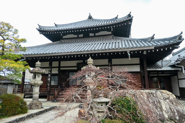 A classic Buddhist temple hall with an elegant tiled roof stands in a quiet garden featuring...