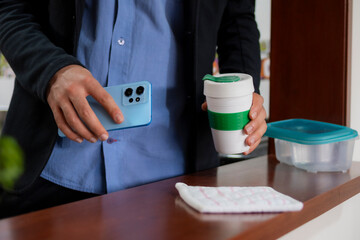Someone taking a green and white portable cup with coffee and smartphone. The scene includes...