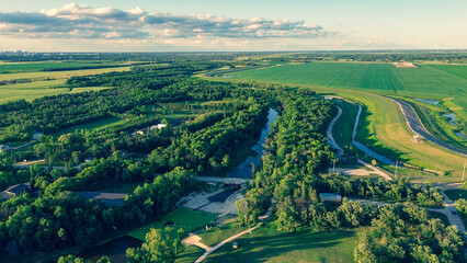 Epic aerial photo of a vast river valley with lush forests, green farmland, and a city skyline on the distant horizon at sunset.