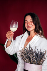 Happy woman in bathrobe holding glass of tasty dairy drink on red background. 