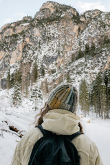A woman wearing a colorful hat and a backpack is standing in the snow