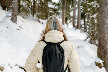 A woman wearing a knit hat and a black backpack is walking through the snow