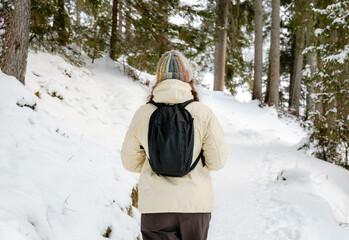 A woman wearing a black backpack is walking through the snow