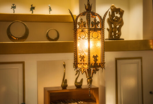 Elegant mid-century hanging lantern with ornate metalwork glows warmly in a vintage living room surrounded by eclectic decor and retro silhouettes—perfect for nostalgic design themes.