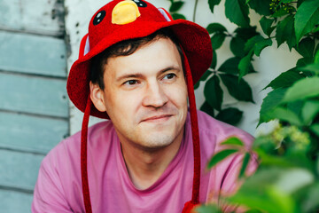 The individual sits against a wall adorned with greenery wearing a bright red hat and a pink shirt...
