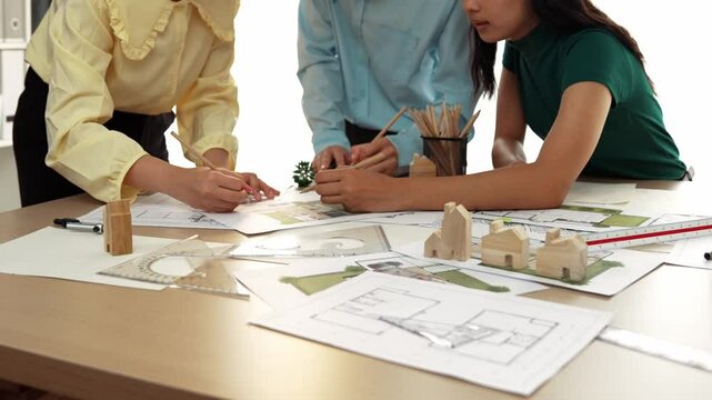 Smart architect and safety engineer discussion about building blueprint on table with architectural document, measurement tools and wooden block scatter around at modern office. Closeup. Delineation.