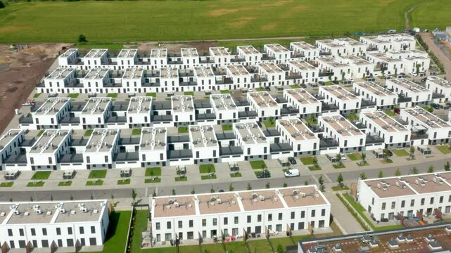 This oblique aerial sequence surveys a grid of modern white townhouses with manicured lawns and service roads under summer light, illustrating residential development planning.