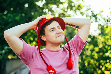 A young man smiles contently while wearing a vibrant red hat in a sunny outdoor setting He relaxes...