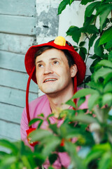 A man dressed in a pink shirt smiles while wearing a playful red hat with cute ears He is...