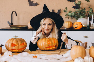 Young woman wearing witch costume carving Halloween pumpkins