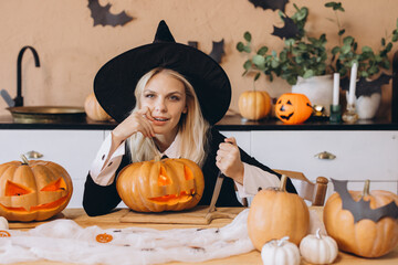 Young woman wearing witch costume carving pumpkins for Halloween party