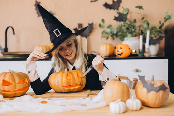 Young woman carving Halloween pumpkins wearing witch costume