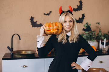 Woman wearing witch costume holding jack o' lantern in Halloween decorated kitchen