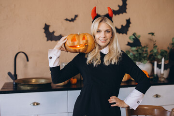 Woman wearing witch costume holding jack o' lantern in halloween decorated kitchen