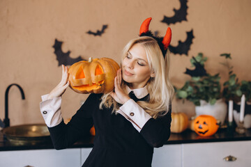Woman wearing witch costume holding jack o' lantern in Halloween decorated kitchen