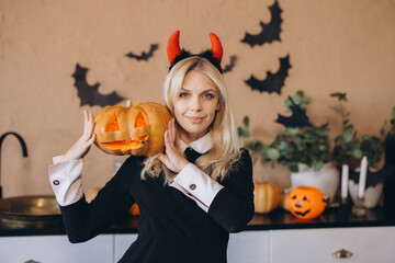 Woman wearing devil costume holding jack o' lantern celebrating Halloween
