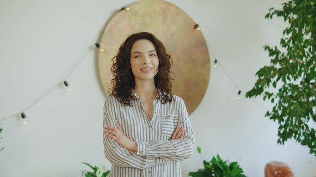 Smiling woman standing confidently in a bright room adorned with plants and warm lights, showcasing a relaxed yet professional atmosphere