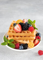 Stack of crispy Belgian waffles with raspberries, blackberries and blueberries on a gray background. 