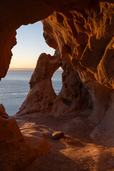 Sunlight casts a warm glow inside a rocky coastal cave, highlighting its unique formations and offering a stunning view of the ocean horizon