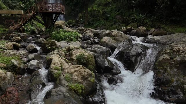Scenic drone view of Gitgit waterfall and a stream flowing over rocks in a lush, natural setting