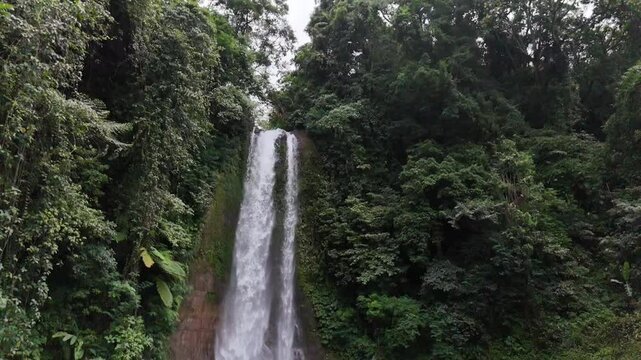 Slow motion drone view of Gitgit waterfall and a stream flowing over rocks in a lush natural setting