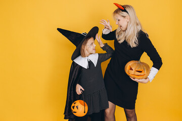 Mother and Daughter Wearing Halloween Costumes Playing with Pumpkins on Yellow Background